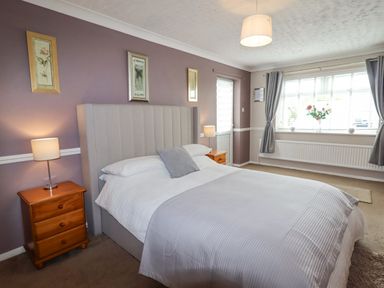 A bedroom with a bed a wooden bedside table with lamps and a window with curtains at Beach Cottage in Conwy