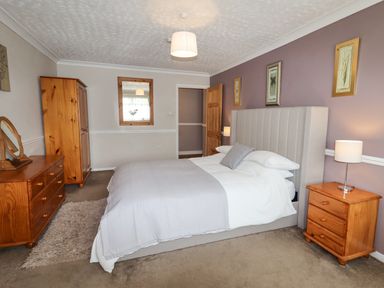 A bedroom with a bed a mirror a wardrobe a chest of drawers and bedside tables at Beach Cottage in Conwy