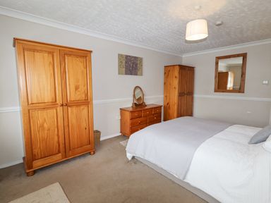 A bedroom with a bed two wooden wardrobes a wooden dresser with a mirror a wall mirror and a painting at Beach Cottage in Conwy