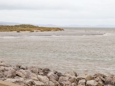 A rocky shoreline with water and a grassy sand dune in the background at Beach Cottage in Conwy