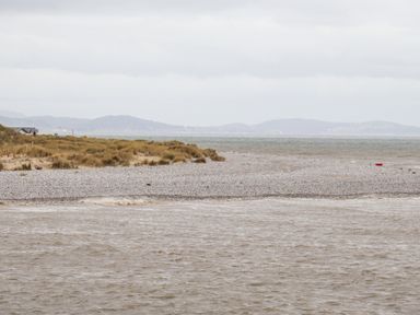 A pebble beach with brown grass dunes and a body of water under a cloudy sky at Beach Cottage in Conwy