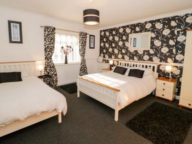 A bedroom with two beds bedside tables lamps a window with patterned curtains and floral wallpaper at Beach Cottage in Conwy