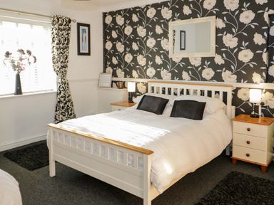 A bedroom with a double bed two nightstands with lamps floral wallpaper and a window with curtains at Beach Cottage in Conwy