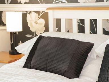 A bed with white bedding and black pillows next to a wooden nightstand with a lamp in a bedroom at Beach Cottage in Conwy