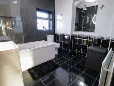 A bathroom with a bathtub toilet sink large mirror and black and white tiled walls and floor at Beach Cottage in Conwy