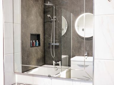 A bathroom with a bathtub shower combination and a vanity with a circular mirror at Beach Cottage in Conwy