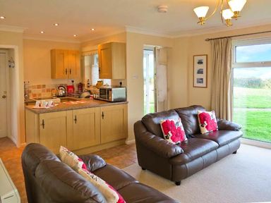 A living room area with two leather sofas with floral cushions next to a kitchen with wooden cabinets at Sunrise Kessingland near Lowestoft