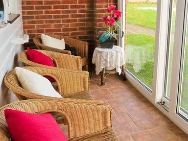 A sunroom with wicker chairs with red and white cushions and a small table with a flower pot at Sunrise in Kessingland near Lowestoft