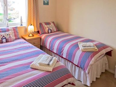 A bedroom with two single beds with striped bedding and a bedside table with a lamp at Sunrise in Kessingland near Lowestoft