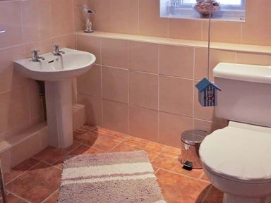 A bathroom with a pedestal sink a toilet a window small trash can and a bath rug at Sunrise in Kessingland near Lowestoft