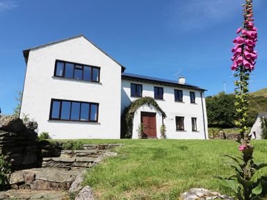 A white two story house with multiple windows a wooden front door and stone steps leading to it at Ghyll Bank House in Staveley near Windermere