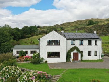 A white house with solar panels on the roof surrounded by a garden and hills at Ghyll Bank House in Staveley near Windermere