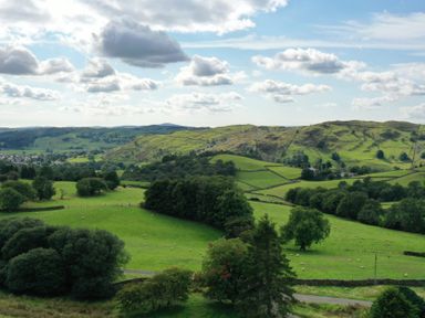 A landscape of green fields with trees and hills under a partly cloudy sky at Ghyll Bank House in Staveley near Windermere