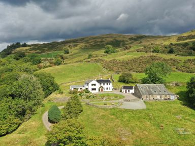 A rural farmhouse with outbuildings on green hills under cloudy sky at Ghyll Bank House in Staveley near Windermere