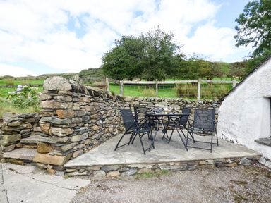 An outdoor patio area with a stone wall and black metal table and chairs at Ghyll Bank Bungalow in Staveley near Windermere