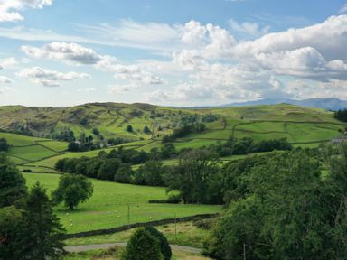 A landscape of green fields with trees and stone walls under a cloudy sky at Ghyll Bank Bungalow in Staveley near Windermere