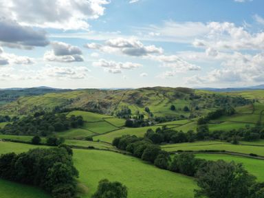A view of green fields with trees and hills under a partly cloudy sky at Ghyll Bank Bungalow Staveley near Windermere