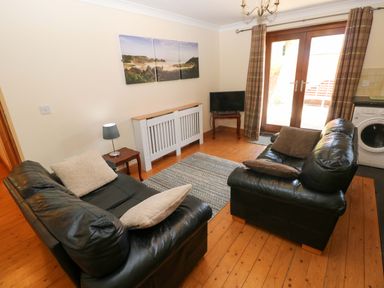 A living room with two sofas, a television, and a door leading outside at The Stall in Penuel near Llanmorlais