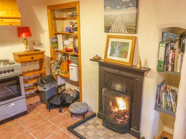 A kitchen corner with a stove a wooden shelf a small fireplace with framed pictures and a wall bookshelf at Willowbrook Cottage in Askill County Leitrim