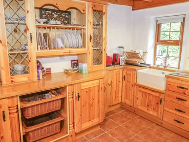 A kitchen with wooden cabinets a white sink dishes on a drying rack and kitchen appliances at Willowbrook Cottage in Askill County Leitrim