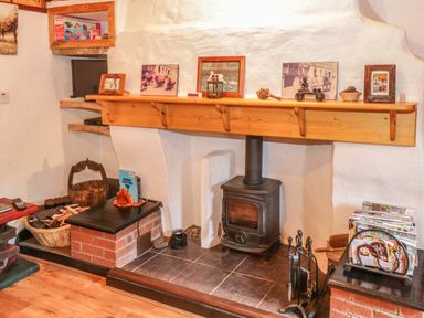 A fireplace with a wood-burning stove and a wooden mantel with framed pictures and decorative items at Willowbrook Cottage in Askill County Leitrim