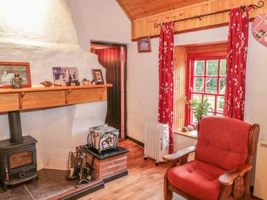 A living room with a wood stove fireplace a red armchair red curtains and a window with plants at Willowbrook Cottage in Askill County Leitrim