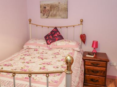 A bedroom with a floral bedspread and pillows a wooden nightstand with a lamp and books at Willowbrook Cottage in Askill County Leitrim