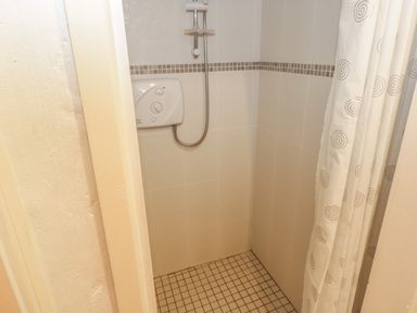 A tiled shower area with a shower unit and a curtain with spiral designs at Willowbrook Cottage in Askill County Leitrim