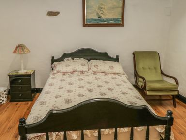 A bedroom with a double bed a floral bedspread a nightstand with a lamp and a green armchair at Willowbrook Cottage in Askill County Leitrim
