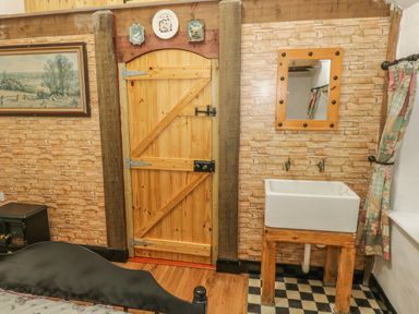 A room with a wooden door sink with wooden frame on checkered floor mirror above sink floral curtain on window and framed picture on wall at Willowbrook Cottage in Askill County Leitrim