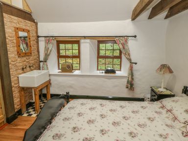 A bedroom with a bed with floral bedding a sink a mirror two windows with curtains and a bedside table with a lamp at Willowbrook Cottage in Askill County Leitrim