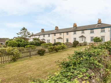 A row of white terraced houses with gardens and picket fences on a grassy slope at Coastguard Cottage in Low Newton-by-the-Sea near Beadnell