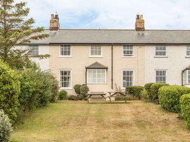 A garden with picnic tables in front of a row of terraced houses at Coastguard Cottage in Low Newton-by-the-Sea near Beadnell