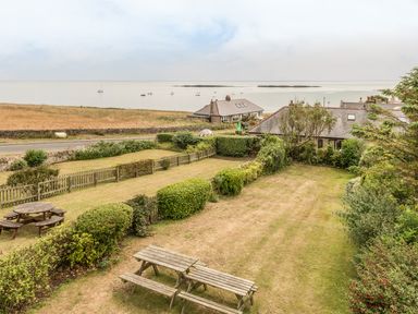A garden with picnic benches and hedges overlooking houses and the sea at Coastguard Cottage in Low Newton-by-the-Sea near Beadnell
