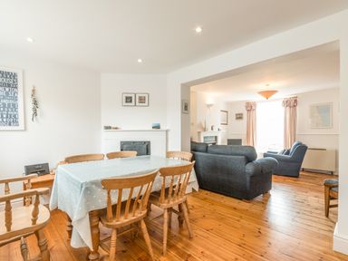 A dining area with wooden chairs and a table with a tablecloth next to a living room with sofas and a large window at Coastguard Cottage in Low Newton-by-the-Sea near Beadnell