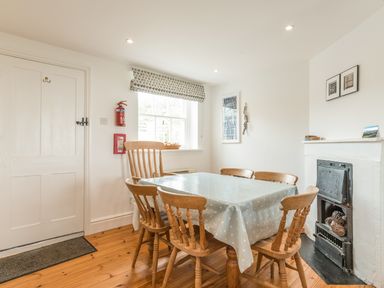 A dining room with wooden chairs around a table covered with a polka dot tablecloth and a fireplace in Coastguard Cottage in Low Newton-by-the-Sea near Beadnell
