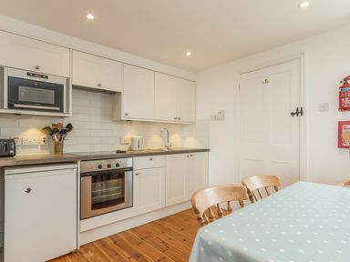 A kitchen with white cabinets wooden chairs a polka dot tablecloth and appliances at Coastguard Cottage in Low Newton-by-the-Sea near Beadnell