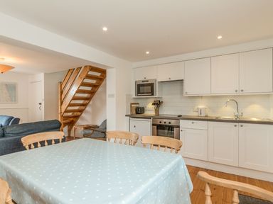 A kitchen and dining area with wooden chairs around a table covered with a blue polka dot tablecloth and a wooden staircase in the background at Coastguard Cottage in Low Newton-by-the-Sea near Beadnell