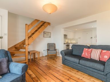 A living room with blue sofas wooden staircase and kitchen area at Coastguard Cottage in Low Newton-by-the-Sea near Beadnell