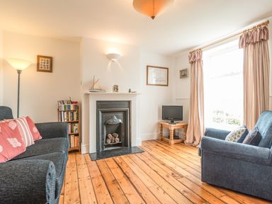 A living room with two blue sofas a fireplace a small tv on a wooden table and wooden floors at Coastguard Cottage in Low Newton-by-the-Sea near Beadnell