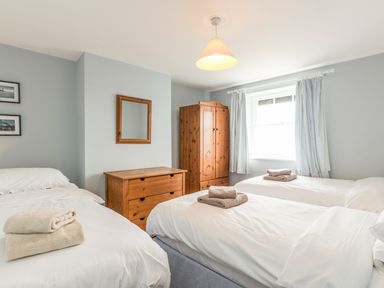 A bedroom with three single beds a wooden chest of drawers a wardrobe and a window with curtains at Coastguard Cottage in Low Newton-by-the-Sea near Beadnell