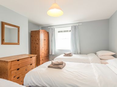 A bedroom with two single beds towels on beds wooden chest of drawers wooden wardrobe and a window with curtains at Coastguard Cottage in Low Newton-by-the-Sea near Beadnell