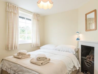 A bedroom with a bed folded towels on it a window with curtains a small fireplace and a mirror on the wall at Coastguard Cottage in Low Newton-by-the-Sea near Beadnell