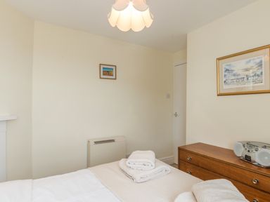 A bedroom with a bed, folded towels, a wooden dresser with a radio, and framed pictures on the wall at Coastguard Cottage in Low Newton-by-the-Sea near Beadnell