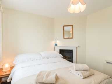 A bedroom with a bed white bedding mirror above a fireplace and towels on the bed at Coastguard Cottage in Low Newton-by-the-Sea near Beadnell