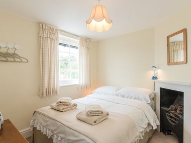 A bedroom with a double bed towels on bed window with curtains and a fireplace at Coastguard Cottage in Low Newton-by-the-Sea near Beadnell