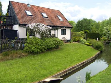 A house with a red tiled roof next to a canal and garden at The Hayloft in Necton near Swaffham