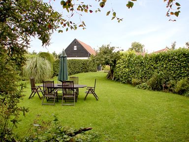 A garden with wooden table and chairs and a closed umbrella surrounded by hedges at The Hayloft in Necton near Swaffham