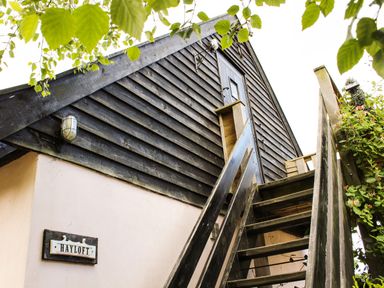 An exterior view of a building with wooden stairs leading to a door and a sign that reads Hayloft at The Hayloft in Necton near Swaffham