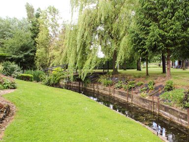 A garden with a small water canal and a bridge over it surrounded by trees at The Hayloft in Necton near Swaffham